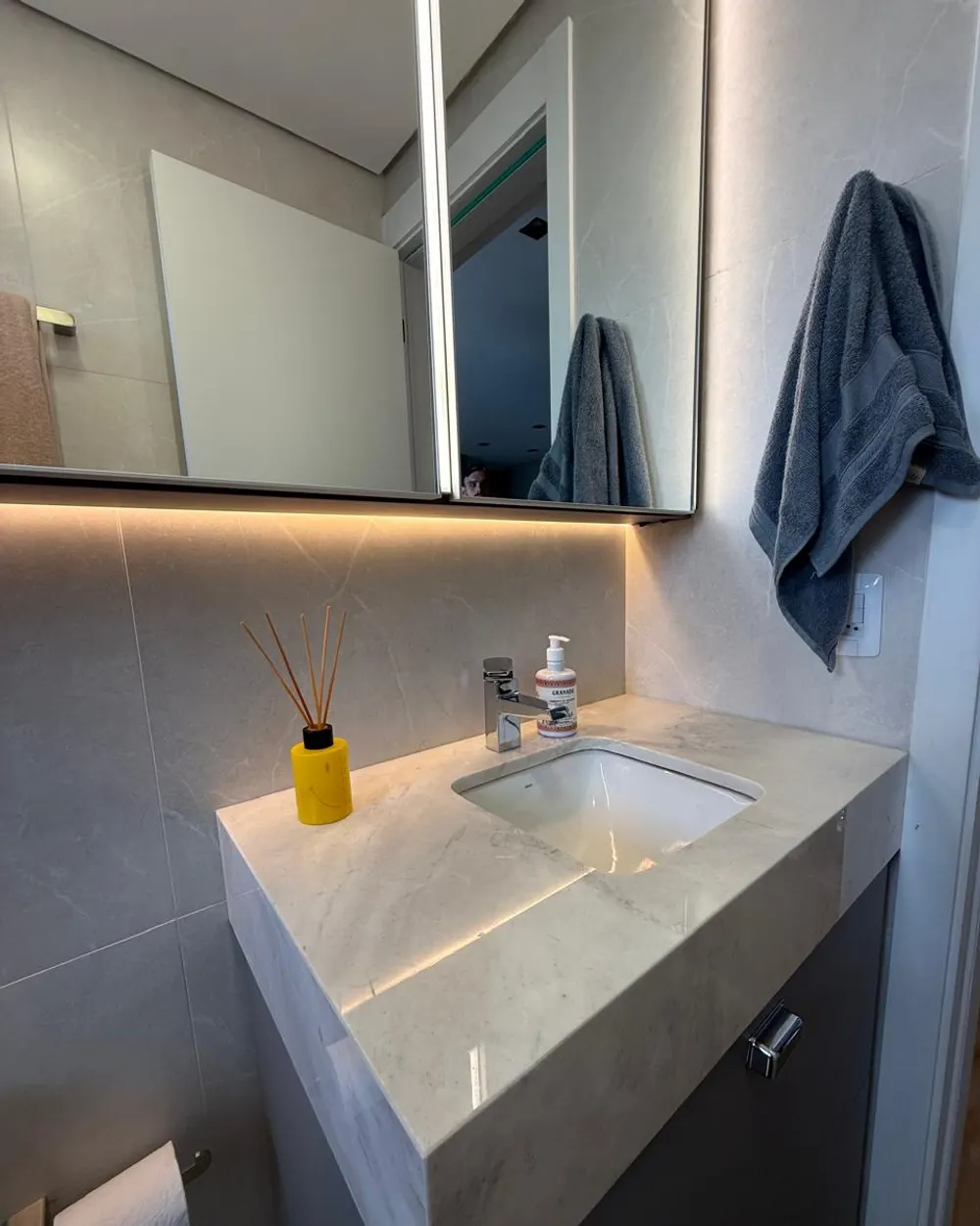 Banheiro com bancada em pedra e espelheira iluminada – Apartamento N+R, Capão da Canoa/RS