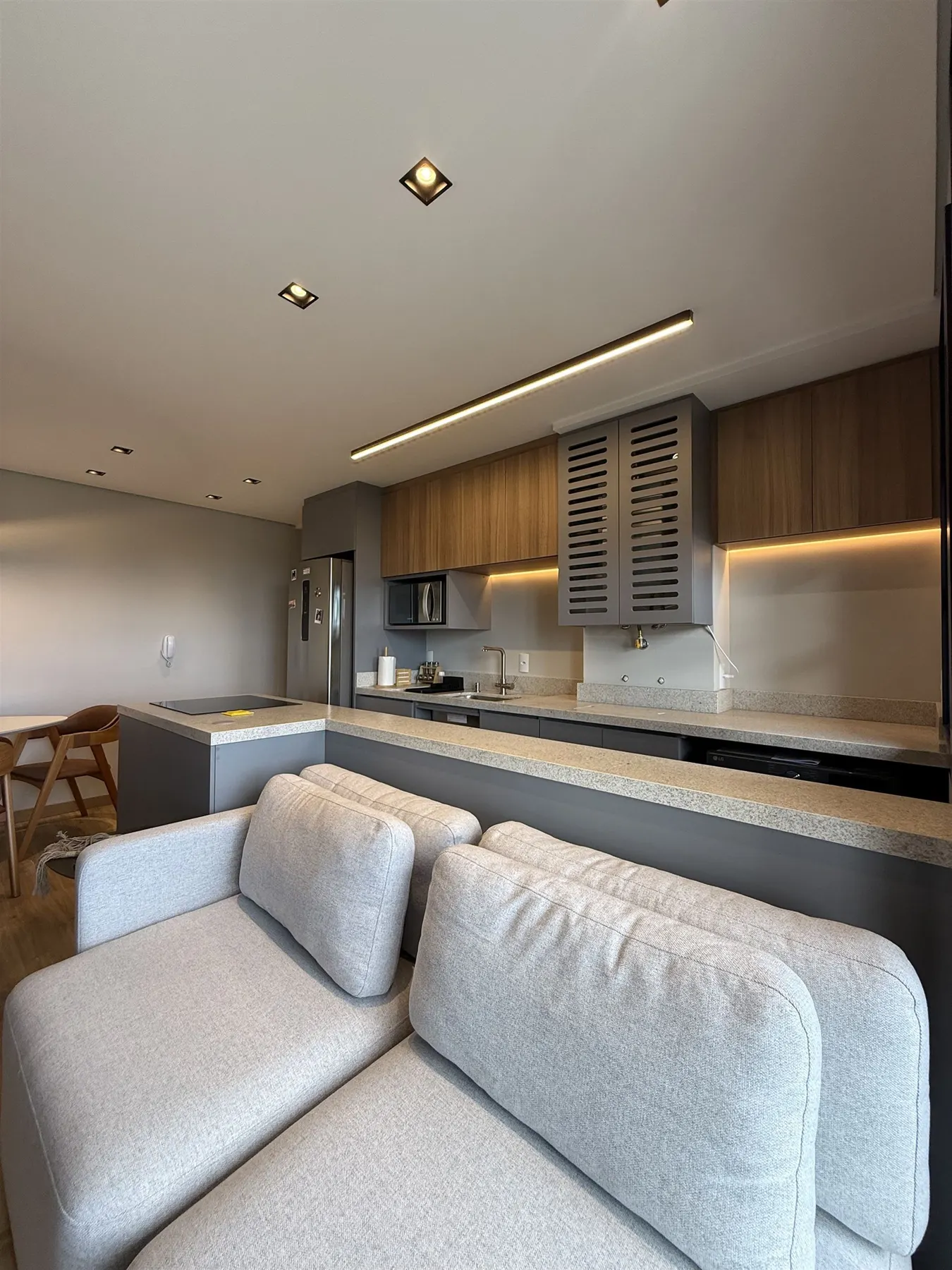 Sala de estar e cozinha integradas do Apartamento N+R, sofá cinza, ilha e marcenaria em tons neutros