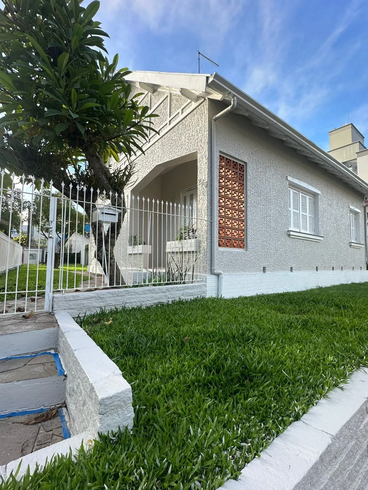 Outro ângulo da fachada repintada, com árvore e grades brancas
