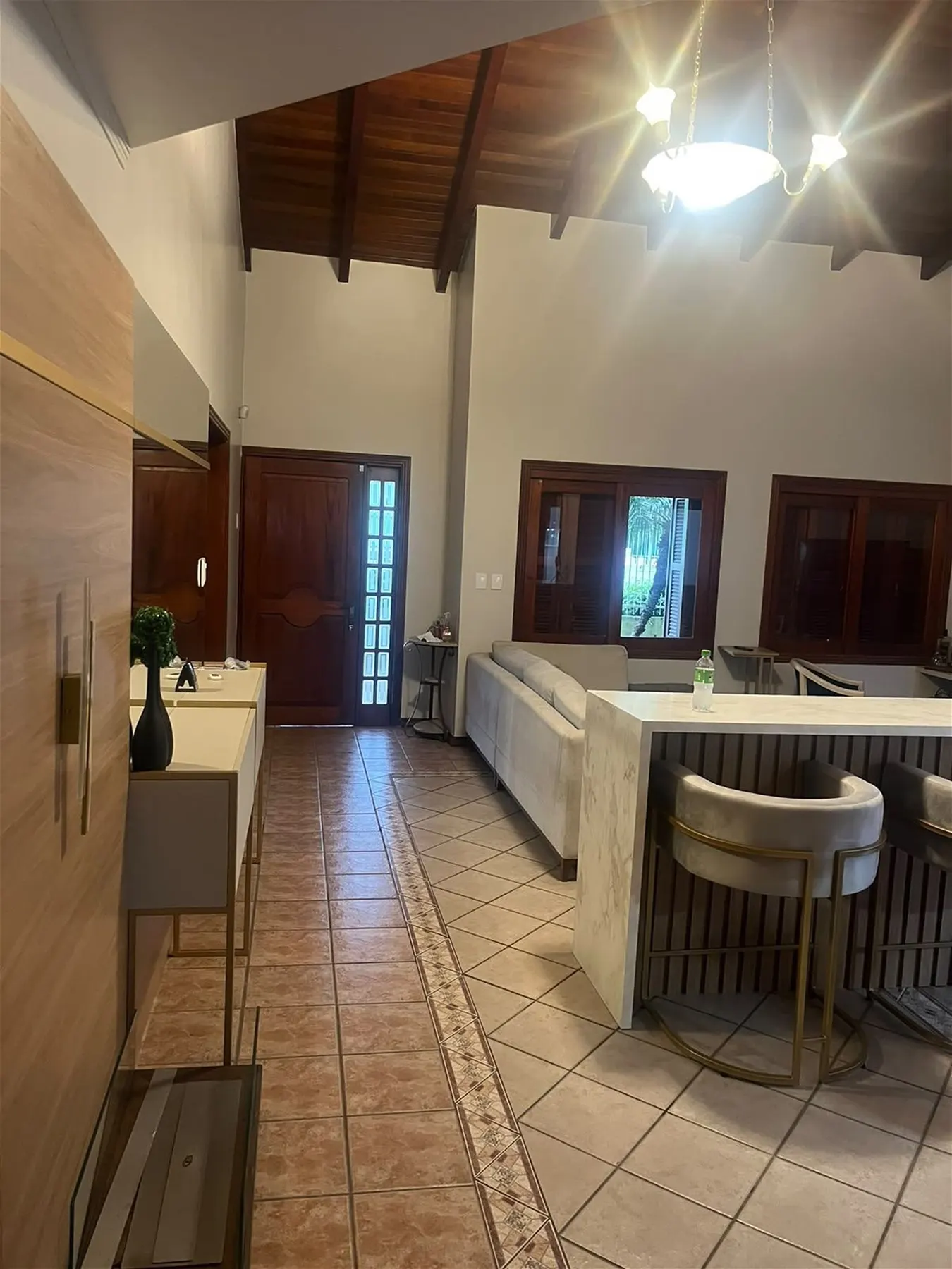 Sala de estar reconstruída, com bar em madeira, banquetas redondas em veludo e teto em telhado aparente
